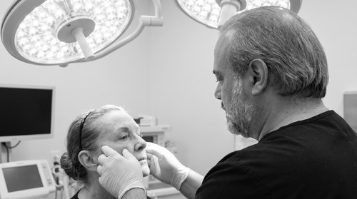 Dr. Frank Agullo, MD, FACS, double board-certified plastic surgeon in El Paso, Texas, in black scrubs in the operating room examining a facelift candidate as part of the preservation-era technique described in his bylined Connectively article.