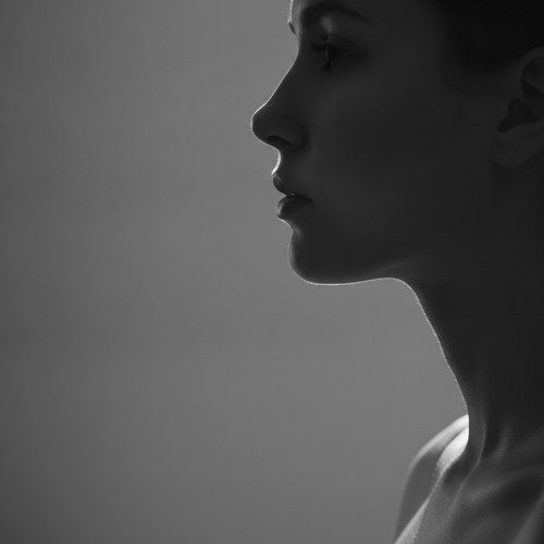 Black and white editorial profile portrait illustrating chin implant facial balance. Surgical commentary by Dr. Frank Agullo, MD, FACS.
