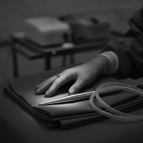 Black and white photo of a gloved surgeon's hand beside a slim handpiece on a surgical drape. Renuvion J-Plasma commentary by Dr. Frank Agullo, MD, FACS.