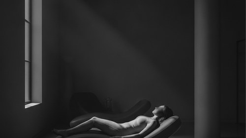 Moody greyscale photograph of a woman resting face down on a recovery lounge in a surgical compression garment. BBL fat survival science explained by Frank Agullo, MD, FACS, Dr. WorldWide.