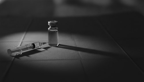 Black and white editorial close-up of a syringe and vial on a sterile surface, illustrating DIY injectables safety commentary by Frank Agullo, MD, FACS.