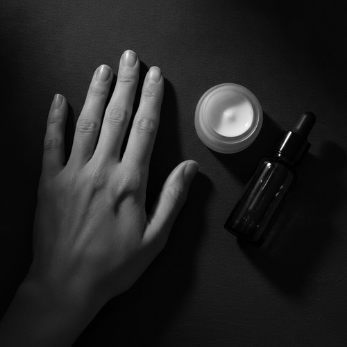 Black and white editorial close-up of a hand with a dropper of serum, illustrating hand skincare prevention commentary by Frank Agullo, MD, FACS.