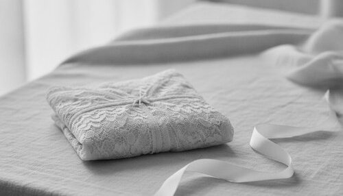 Black and white editorial still life of delicate ivory lace lingerie folded on linen in soft light. Preservé breast augmentation editorial by Dr. Frank Agullo, MD, FACS.