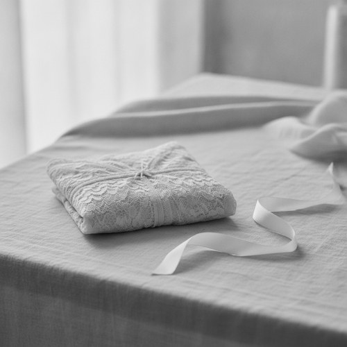 Black and white editorial still life of delicate ivory lace lingerie folded on linen in soft light. Preservé breast augmentation editorial by Dr. Frank Agullo, MD, FACS.