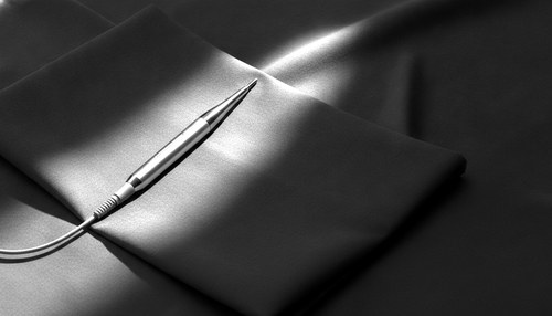 Black and white photograph of a slim electrosurgical handpiece on a folded surgical drape under hard directional light. Renuvion commentary by Frank Agullo, MD, FACS.