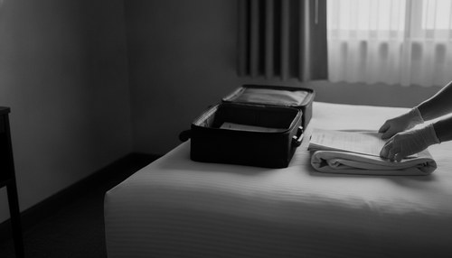 Black and white photograph of a packed carry-on bag and a folded compression garment on a hotel bed. Commentary by Frank Agullo, MD, FACS.