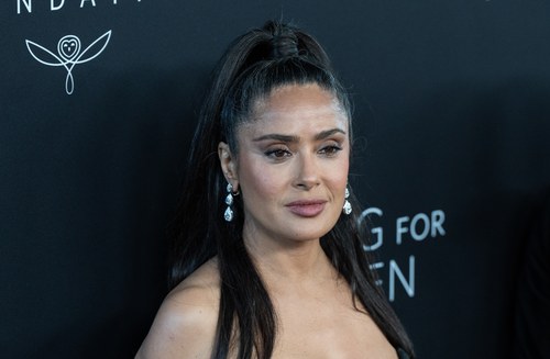 Salma Hayek on the red carpet in September 2025, long dark hair in a high half ponytail, drop diamond earrings, photographed at a three-quarter angle. Commentary by Frank Agullo, MD, FACS.